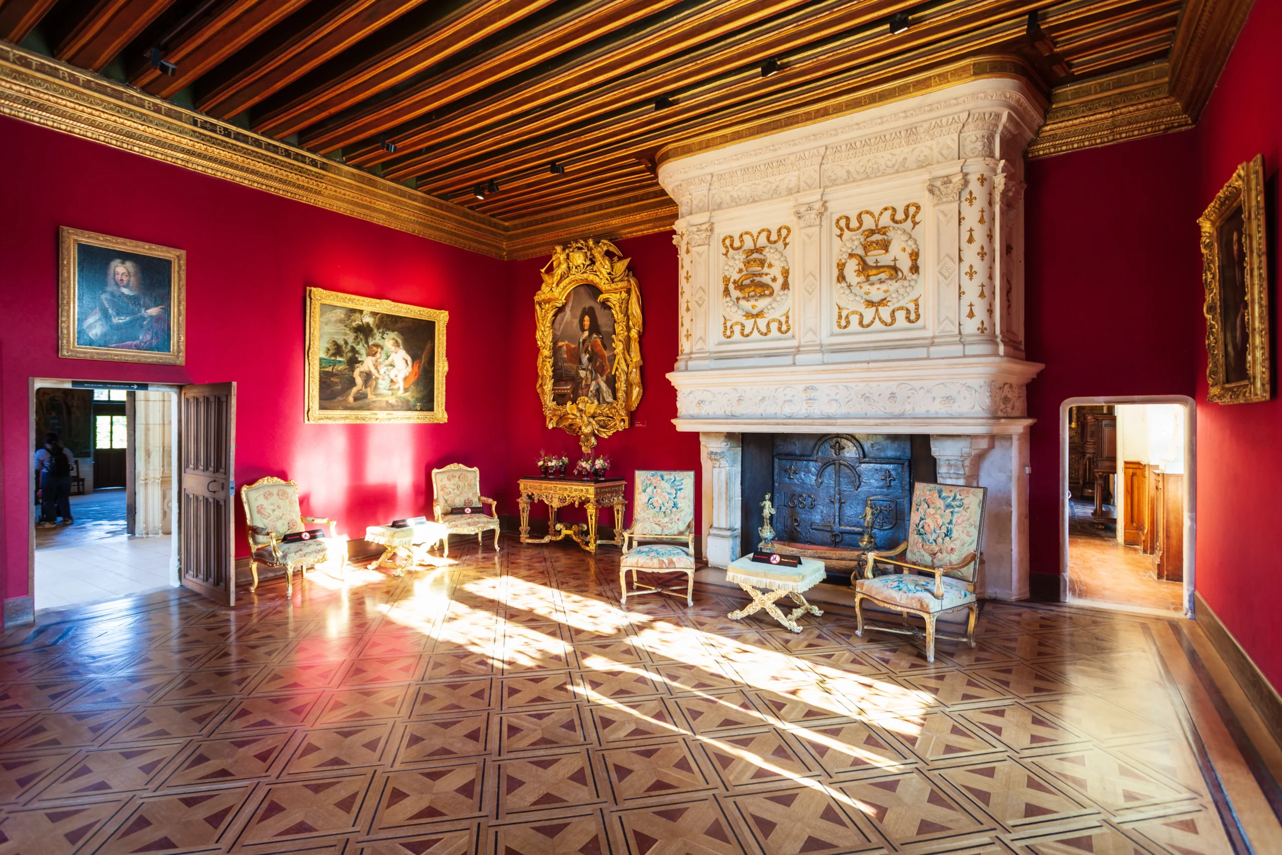 Grand salon du château de Cheverny avec murs rouges, cheminée monumentale sculptée, parquet ancien, mobilier d’époque et tableaux de maîtres.