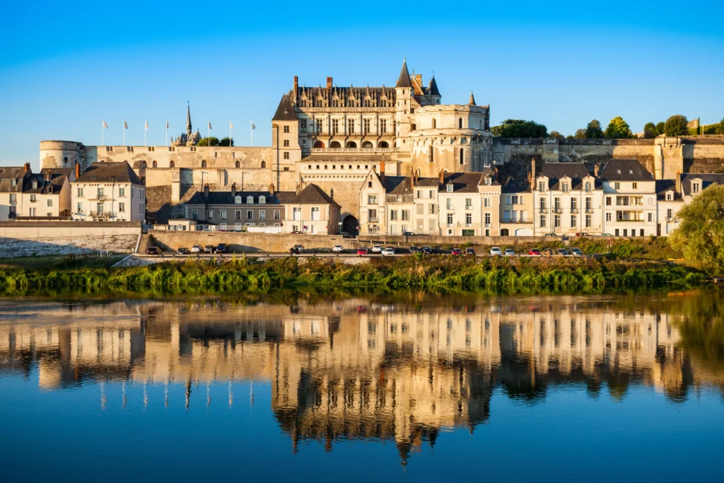 Vue du château royal d’Amboise et des quais de Loire se reflétant dans les eaux calmes du fleuve au coucher du soleil.