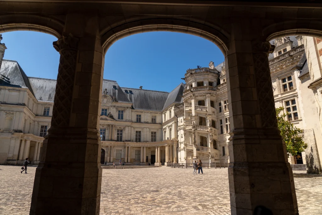 Vue de la cour intérieure du château royal de Blois encadrée par une arcade, mettant en valeur le célèbre escalier Renaissance de l’aile François Ier.