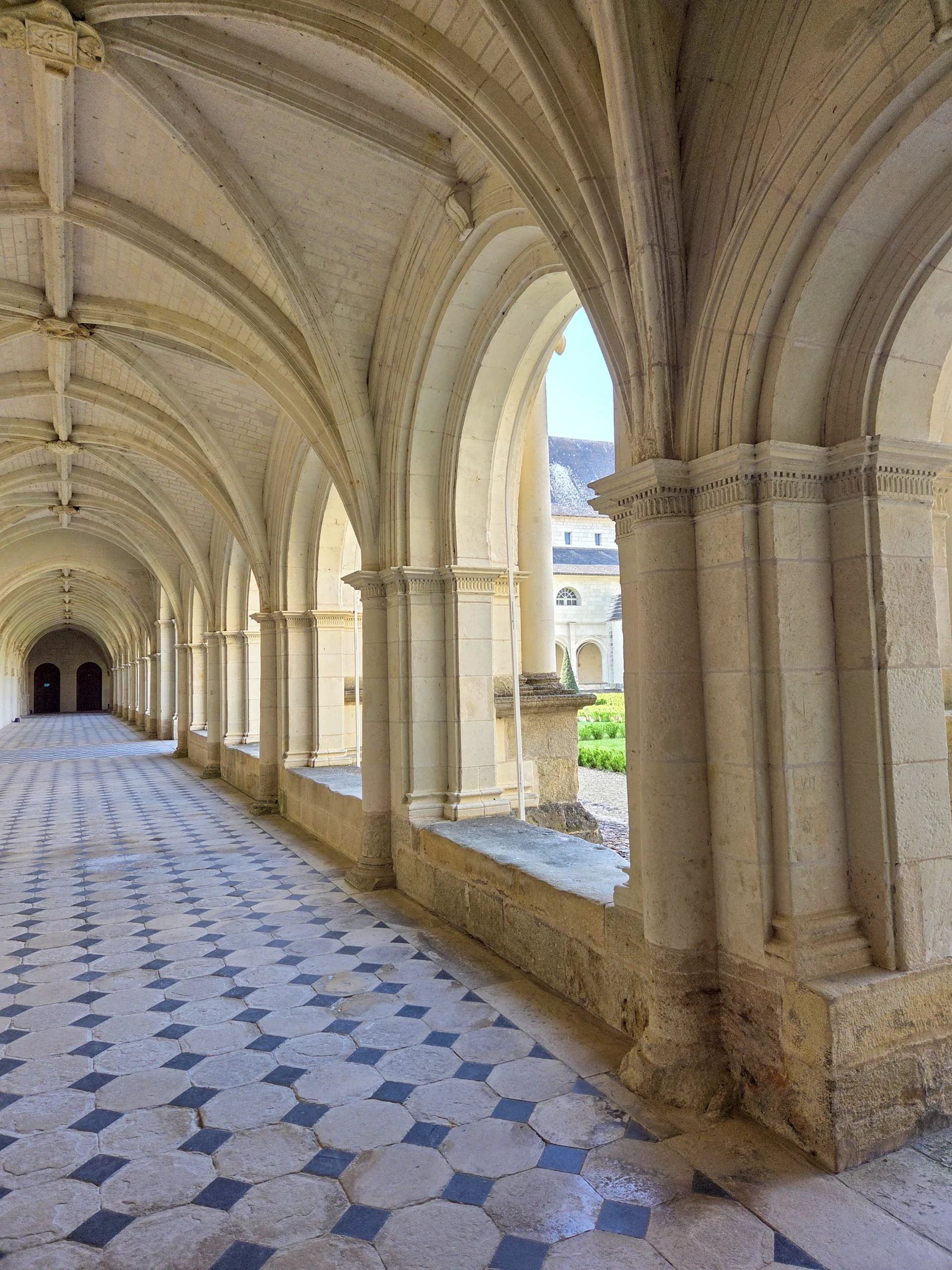 Galerie du cloître de l'Abbaye Royale de Fontevraud avec ses voûtes gothiques et son sol pavé ouvrant sur les jardins monastiques.
